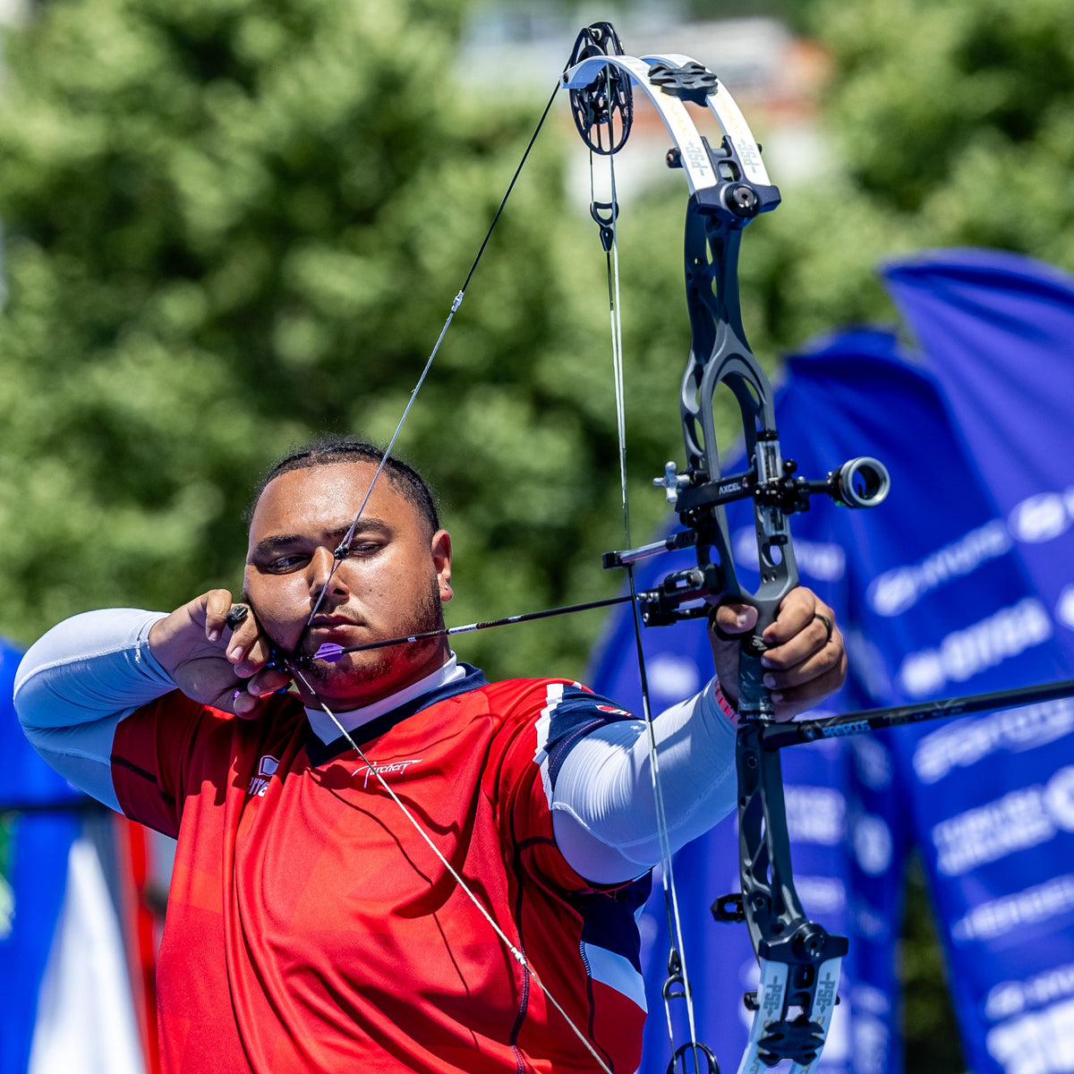 Archer Ajay Scott in red and white outfit with archery equipment, blurred background